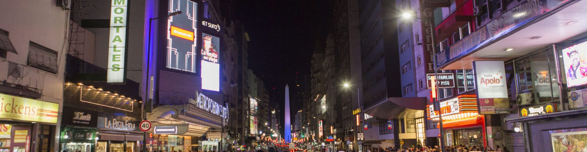 Noche de Calle Corrientes con gente caminando por la calle hecha peatonal, de fondo el obelisco iluminado de menara muy atractiva, Ciudad de Buenos Aires
